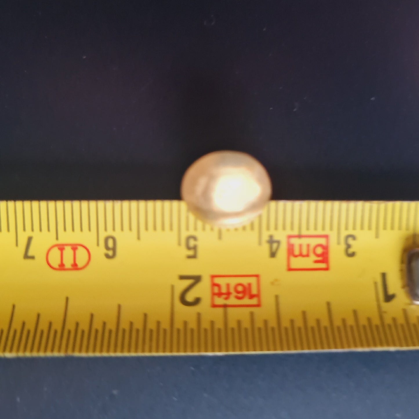 Small round object next to a yellow ruler on a dark background