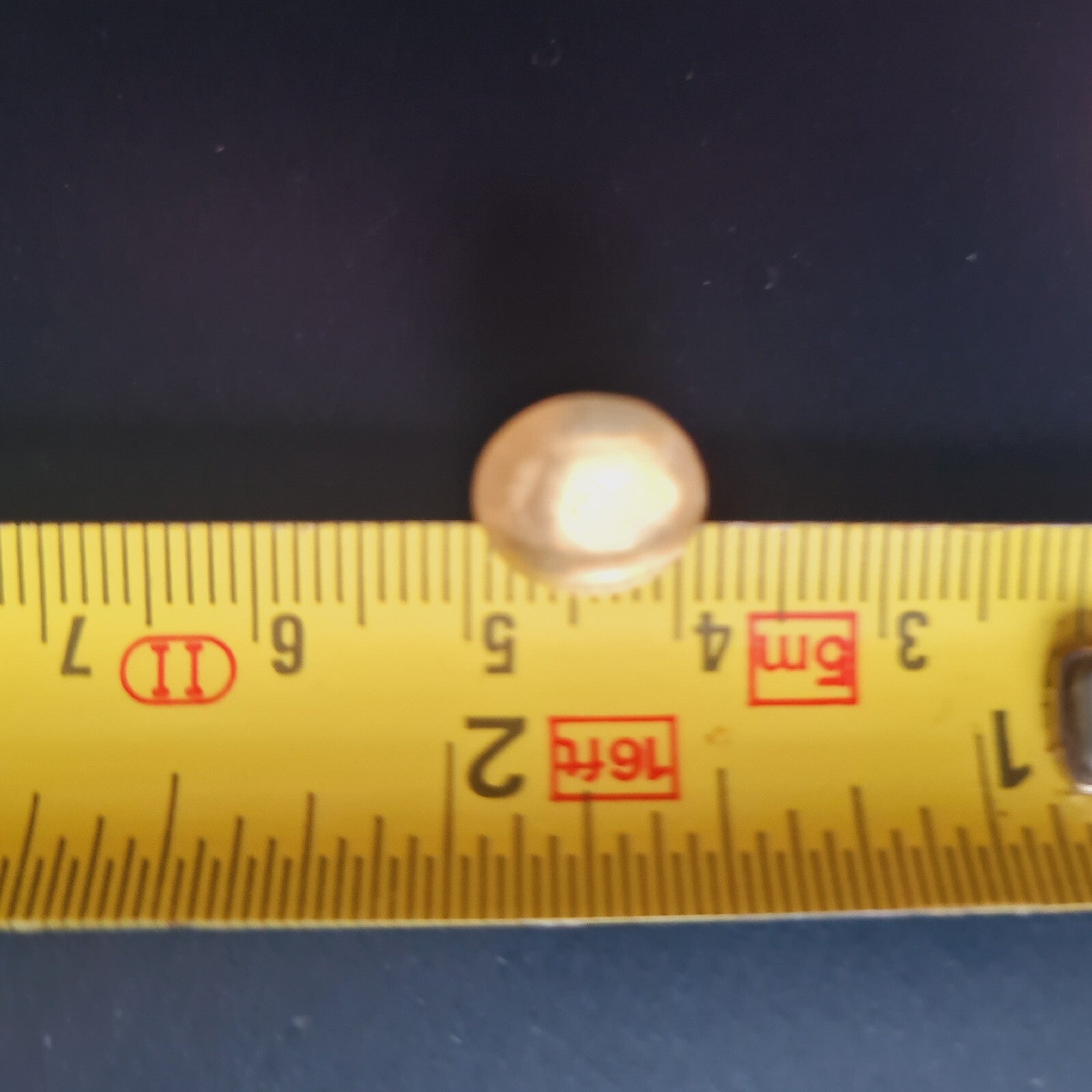 Small round object next to a yellow ruler on a dark background