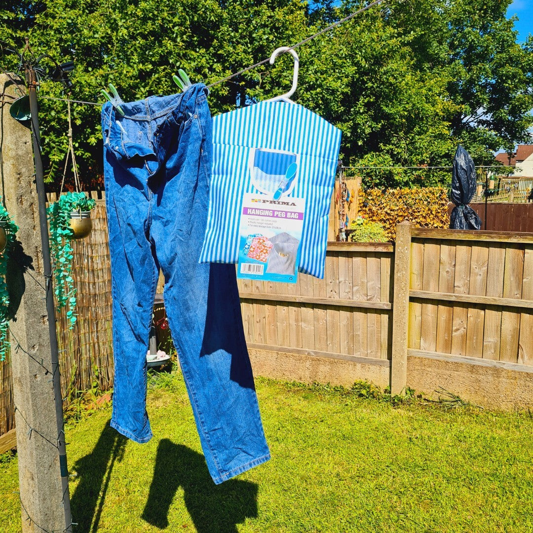 Blue jeans and a striped shirt with a label hanging on a clothesline in a garden.