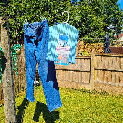 Blue jeans and a striped shirt with a label hanging on a clothesline in a garden.